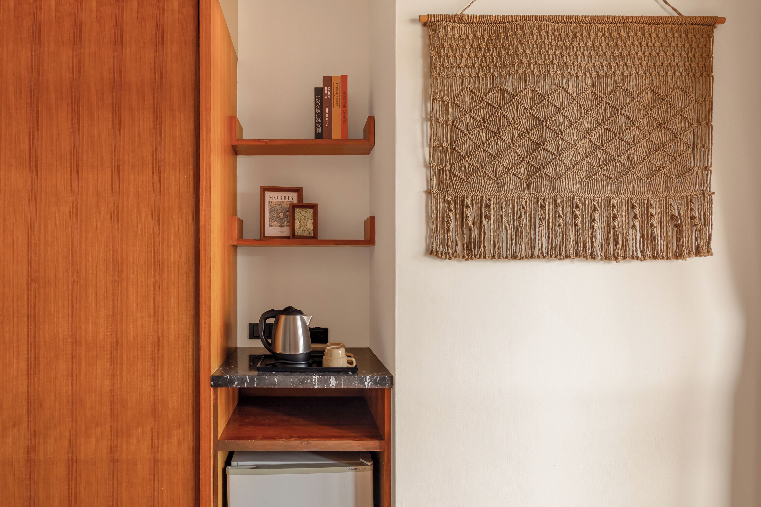 A compact kitchen with wooden shelves, a coffee maker, and a macrame wall hanging.