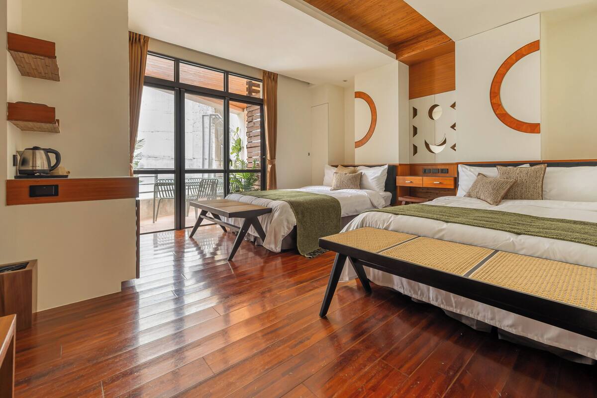 Une chambre d’hôtel avec deux lits, un plancher en bois, un balcon avec vue et un coin cuisine équipé d’une bouilloire.
