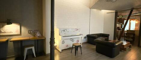 Una sala de estar acogedora con un piano, un sofá de cuero negro y una mesa de centro de madera.