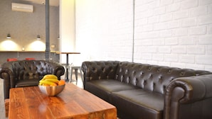 A room with a leather sofa, a wooden coffee table with a fruit bowl, and a white brick wall.
