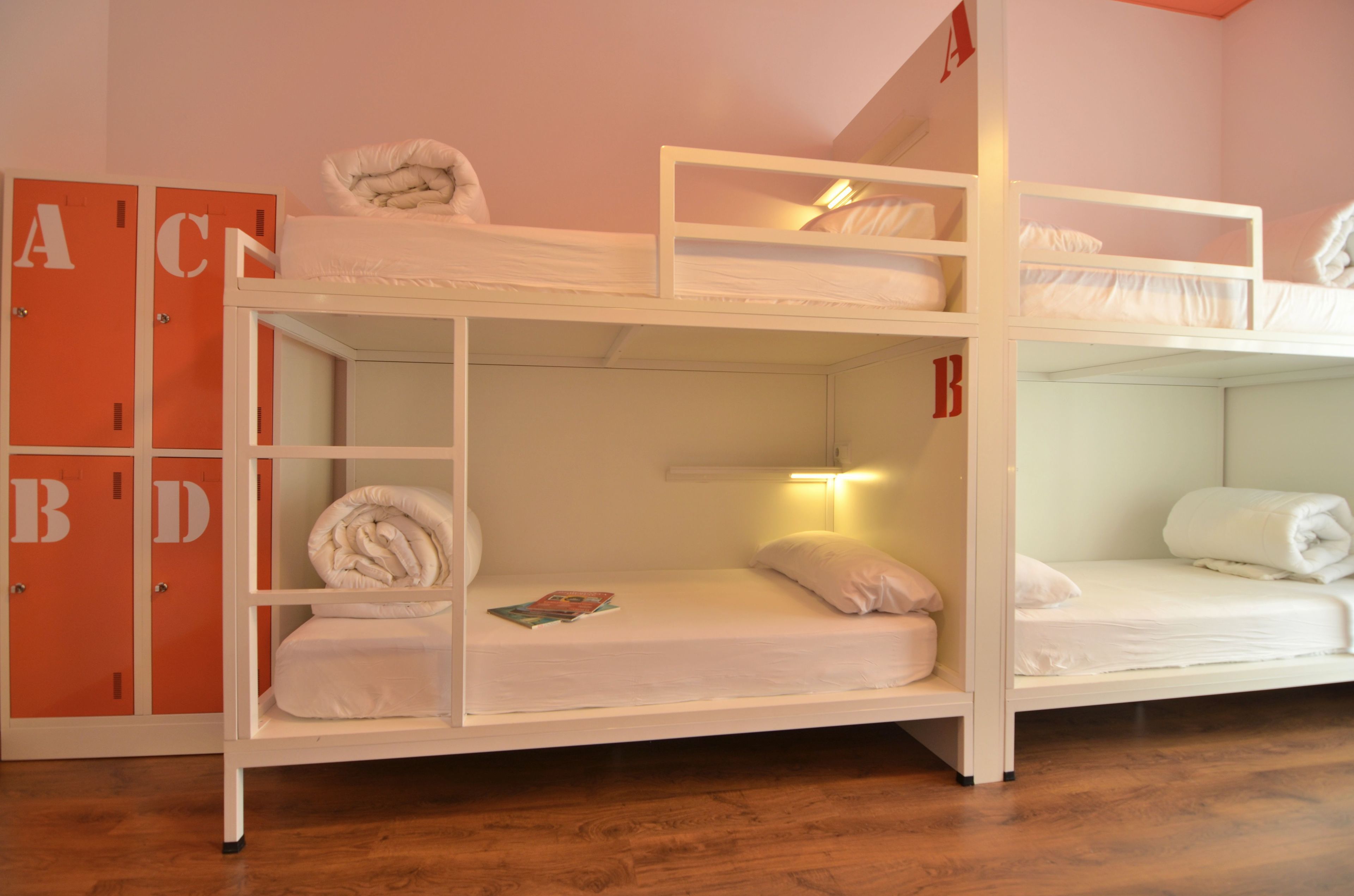 A bunk bed room with a wooden floor, orange lockers, and a magazine on the lower bunk.