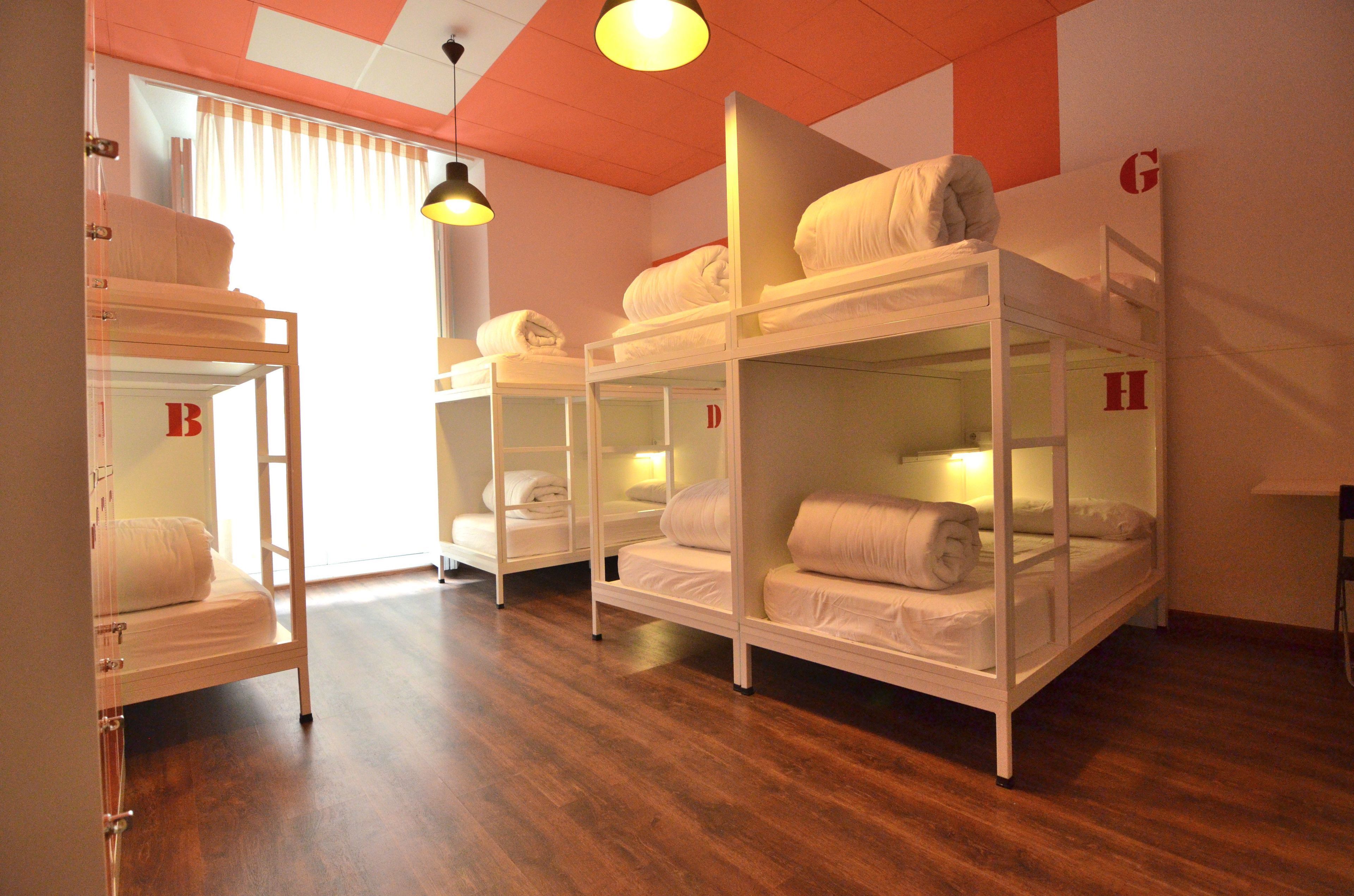 Habitación de hotel con literas, suelo de madera y una ventana con cortinas.
