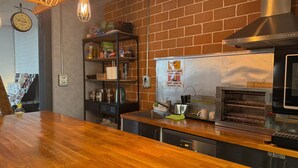 A kitchen with a brick wall, wooden counter, shelves with kitchen items, a clock, and a stainless steel range hood.
