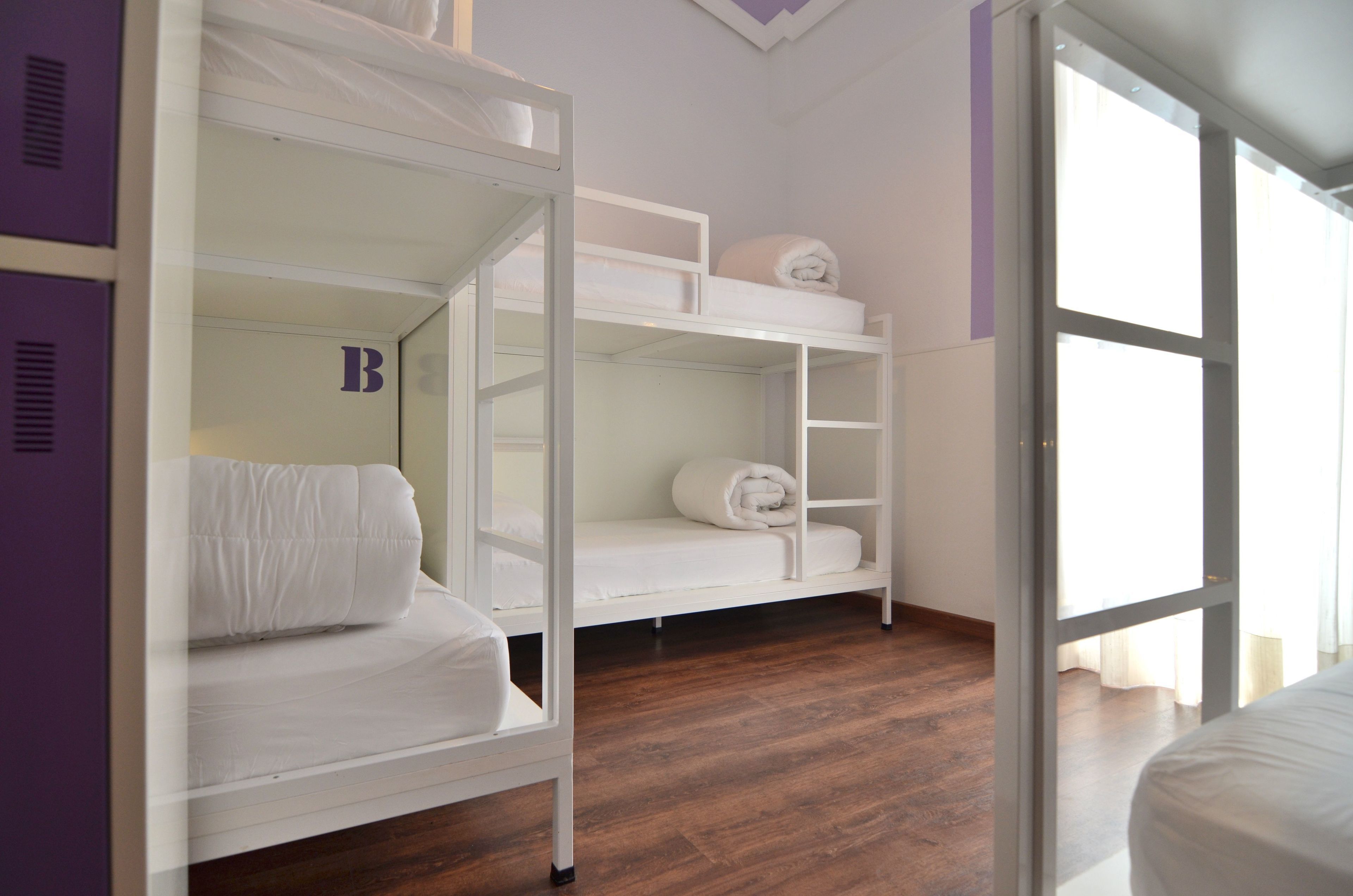 A room with bunk beds, a wooden floor, and a large window.