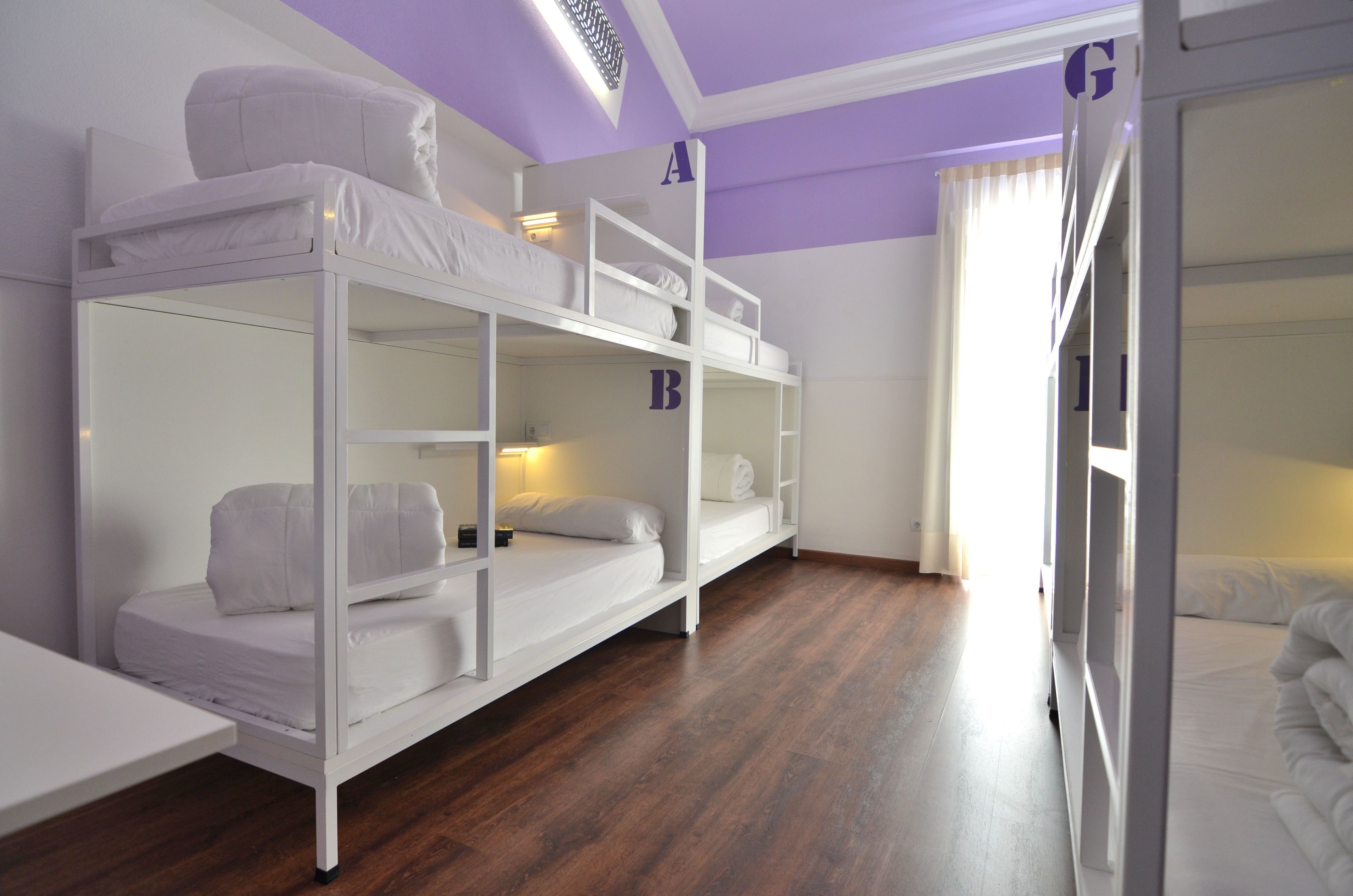 A bunk bed room with a wooden floor, white bedding, and a small table.
