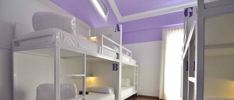 A bunk bed room with a wooden floor, white bedding, and a small table.