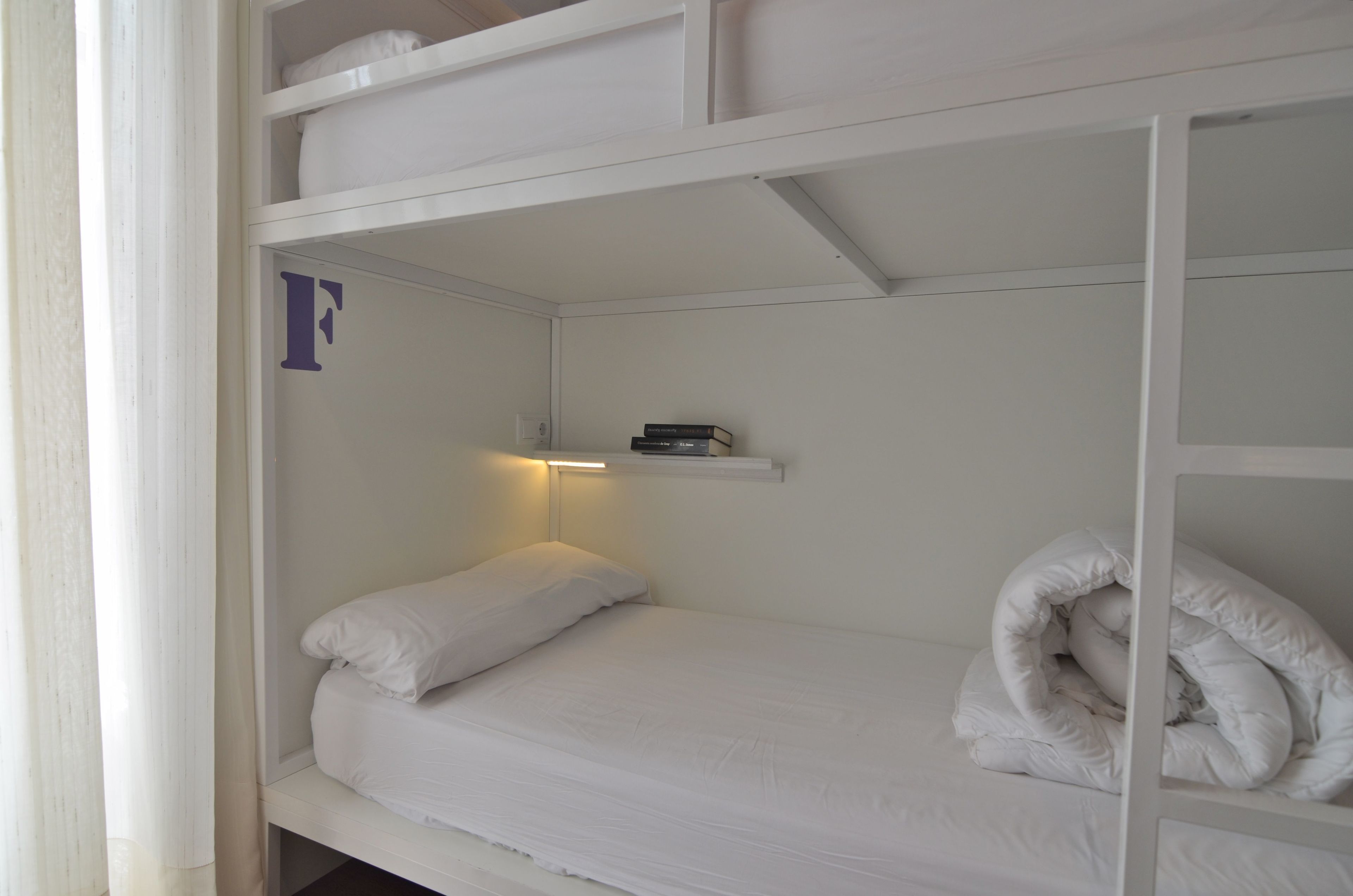 Un letto a castello con ripiano sopra, un cuscino e una coperta arrotolata.