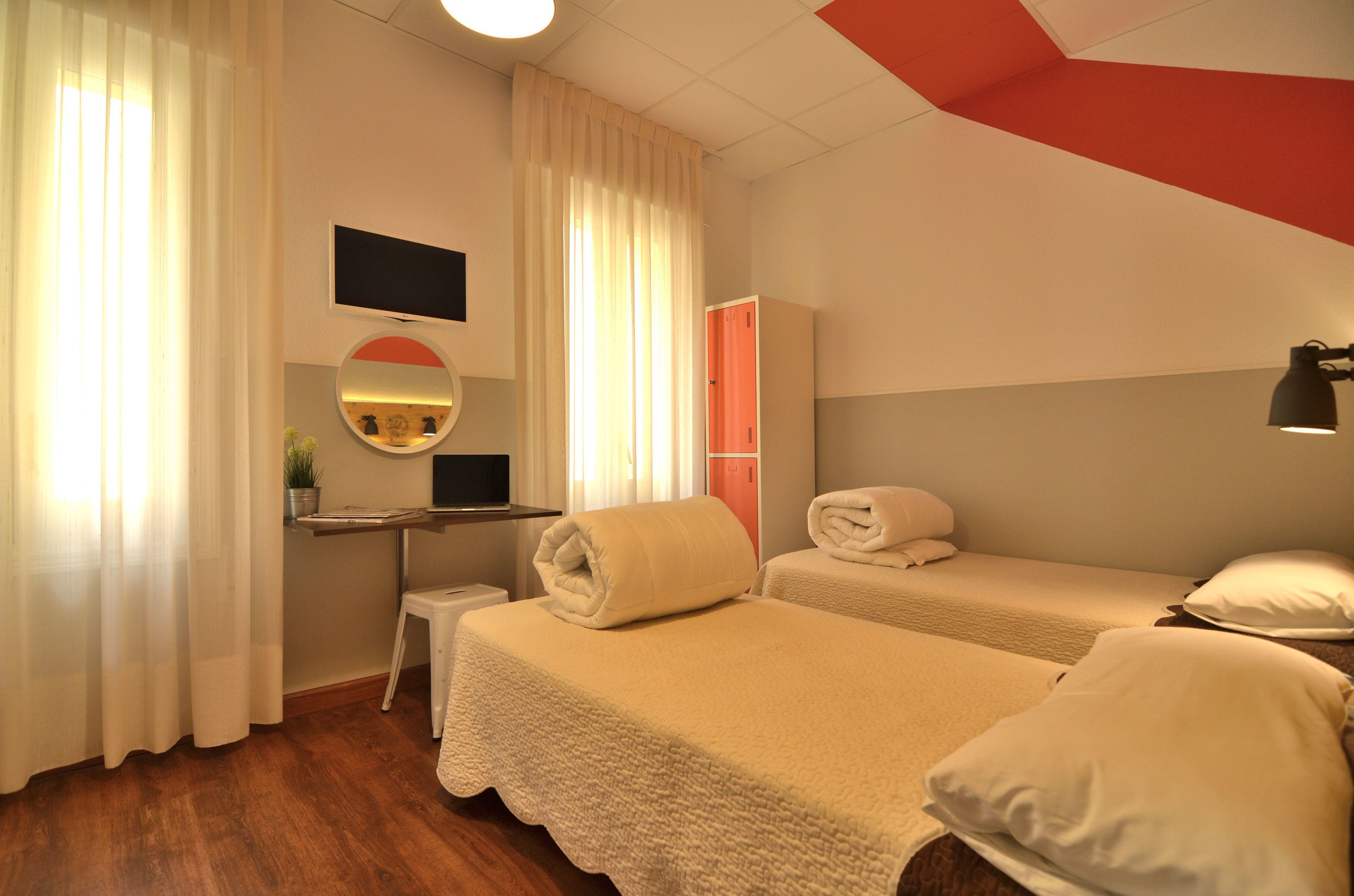 Ein Hotelzimmer mit zwei Betten, einem Schreibtisch, einem Stuhl, einem Fernseher und einem Spiegel.