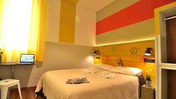A hotel room with a bed, a desk with a laptop, and a window with curtains.