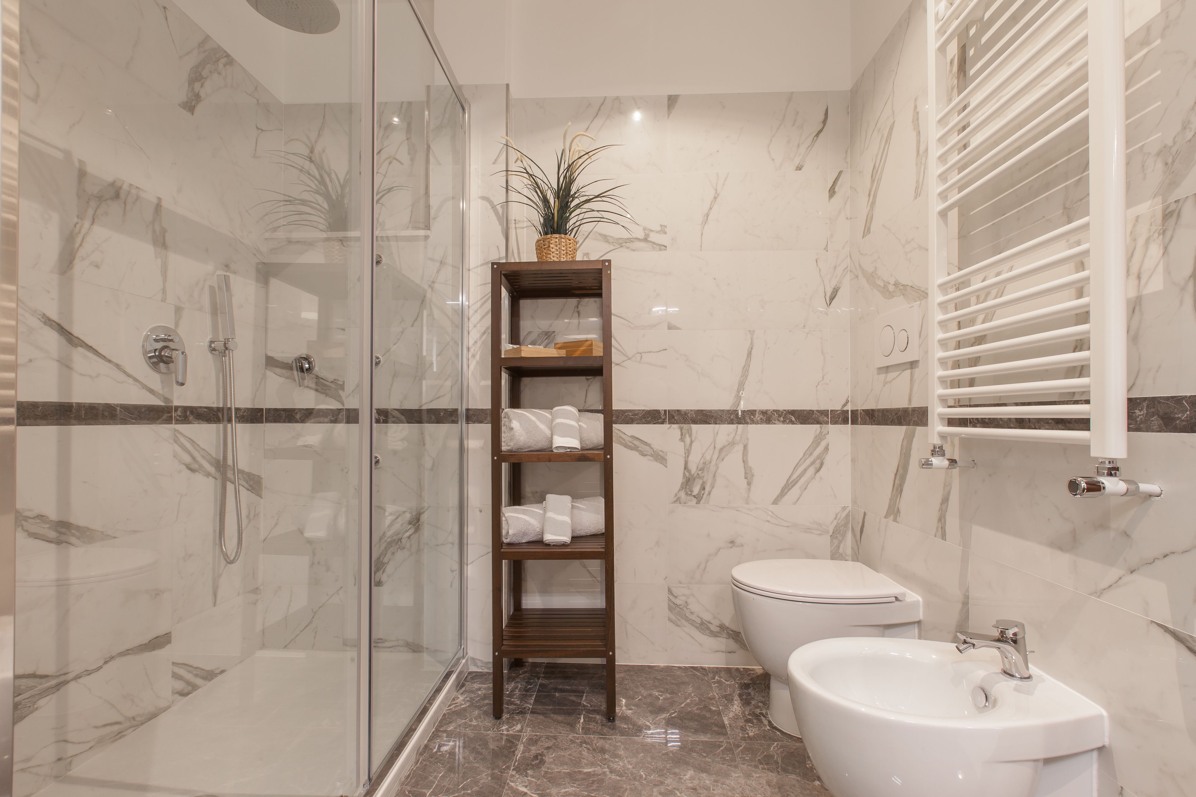 A bathroom with a glass-enclosed shower, a wooden shelf with towels, a toilet, and a sink.