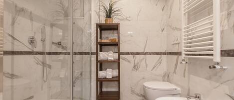 A bathroom with a glass-enclosed shower, a wooden shelf with towels, a toilet, and a sink.