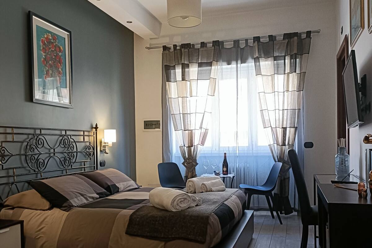 A modern hotel room with a bed, desk, chair, and a painting on the wall.