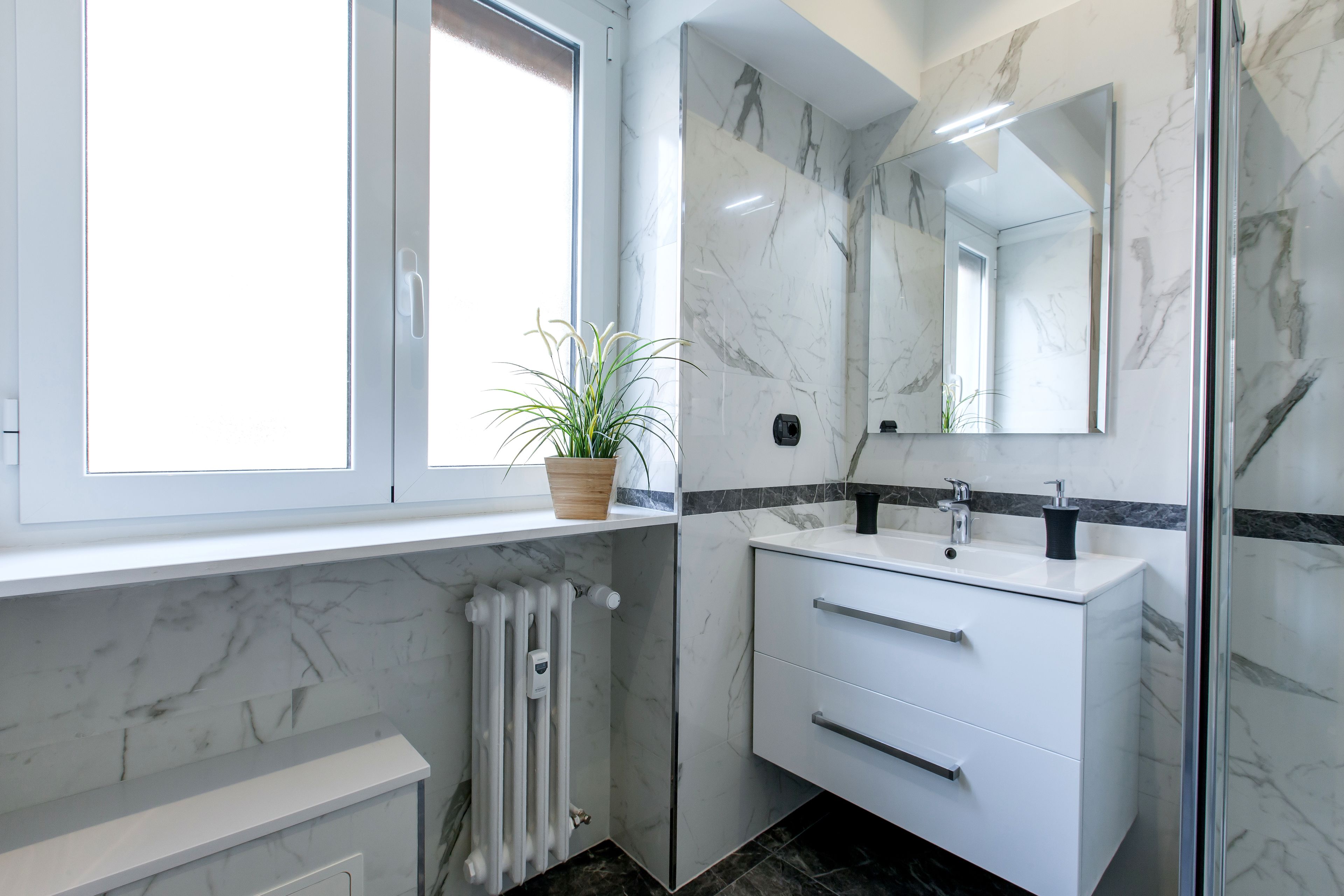 Une salle de bain moderne avec un meuble-lavabo blanc, un grand miroir et une plante en pot.