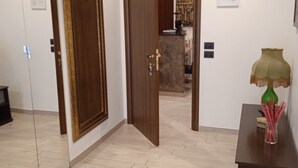 Une chambre d’hôtel avec une porte en bois, un miroir, une petite table avec une lampe et un sol carrelé.