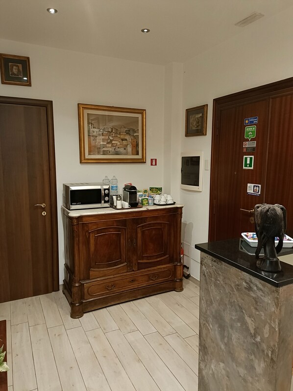 Una cocina con un armario de madera, un microondas y una cafetera. Hay cuadros en la pared y una puerta con un letrero.