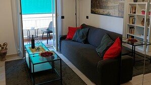 Un salon moderne avec un canapé gris, des coussins rouges, une table basse en verre et une bibliothèque.