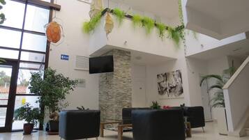 Un vestíbulo espacioso con techos altos, ventanas amplias y una decoración que combina elementos modernos y naturales, como plantas colgantes y obras de arte.