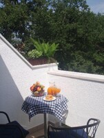 Ein Balkon mit einem Frühstückstisch, gedeckt mit Früchten, einem Croissant und Orangensaft.