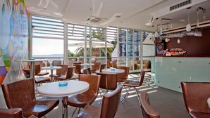 Un ristorante moderno con tavoli rotondi e sedie marroni, ampie finestre e un'area bar con un bancone vetrina.