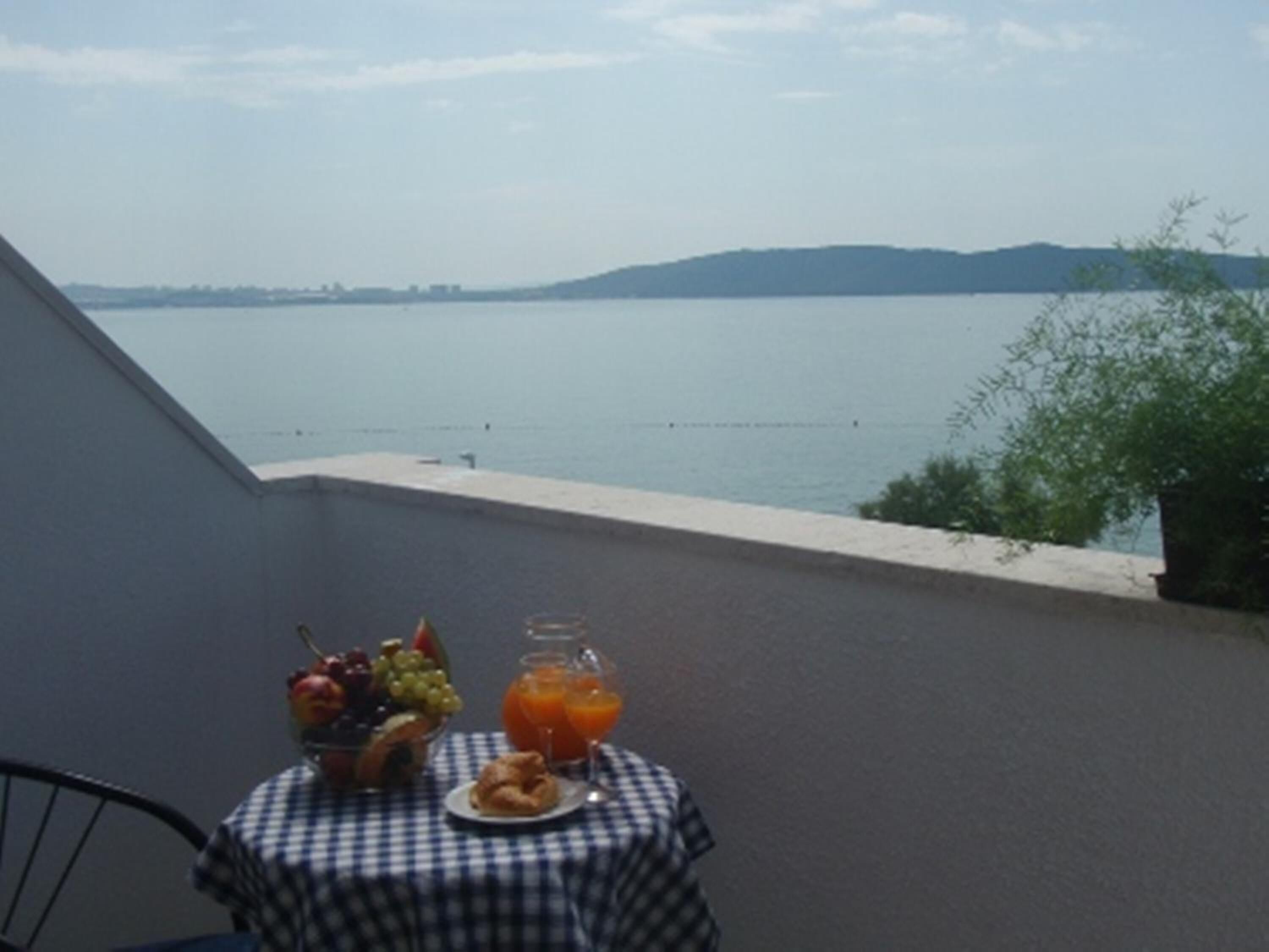 A balcony with a table set for breakfast, overlooking a body of water and distant hills.