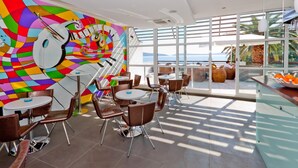 Un ristorante moderno con un murale vivace, tavoli e sedie rotonde, e vista sull'oceano.