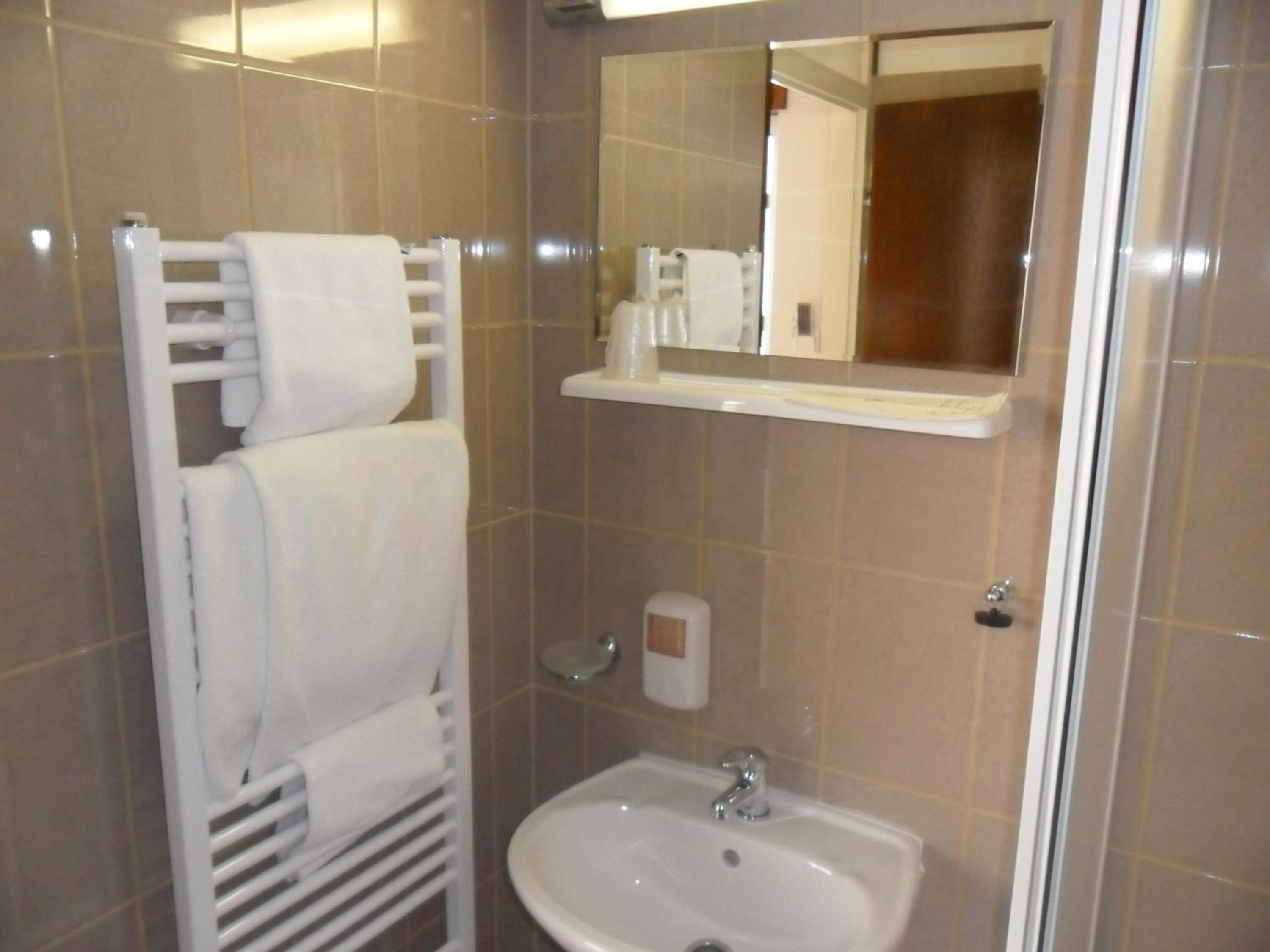Un baño con un lavamanos blanco, un perchero, un espejo y un dispensador de jabón.