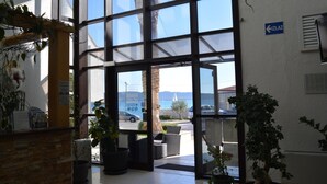 Ingresso di un hotel con ampie vetrate, una reception con piante e vista sul mare e sulle montagne.