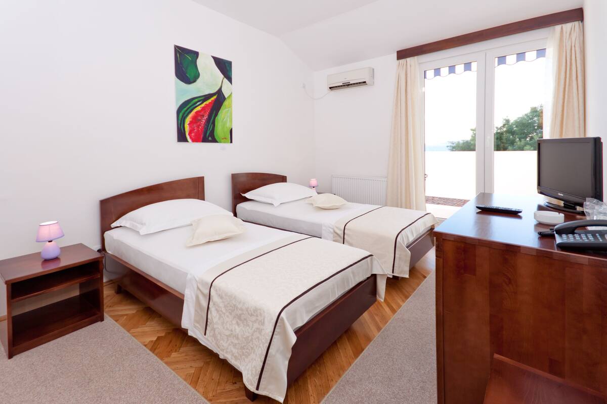 A hotel room with two beds, a desk with a computer, and a window with curtains.