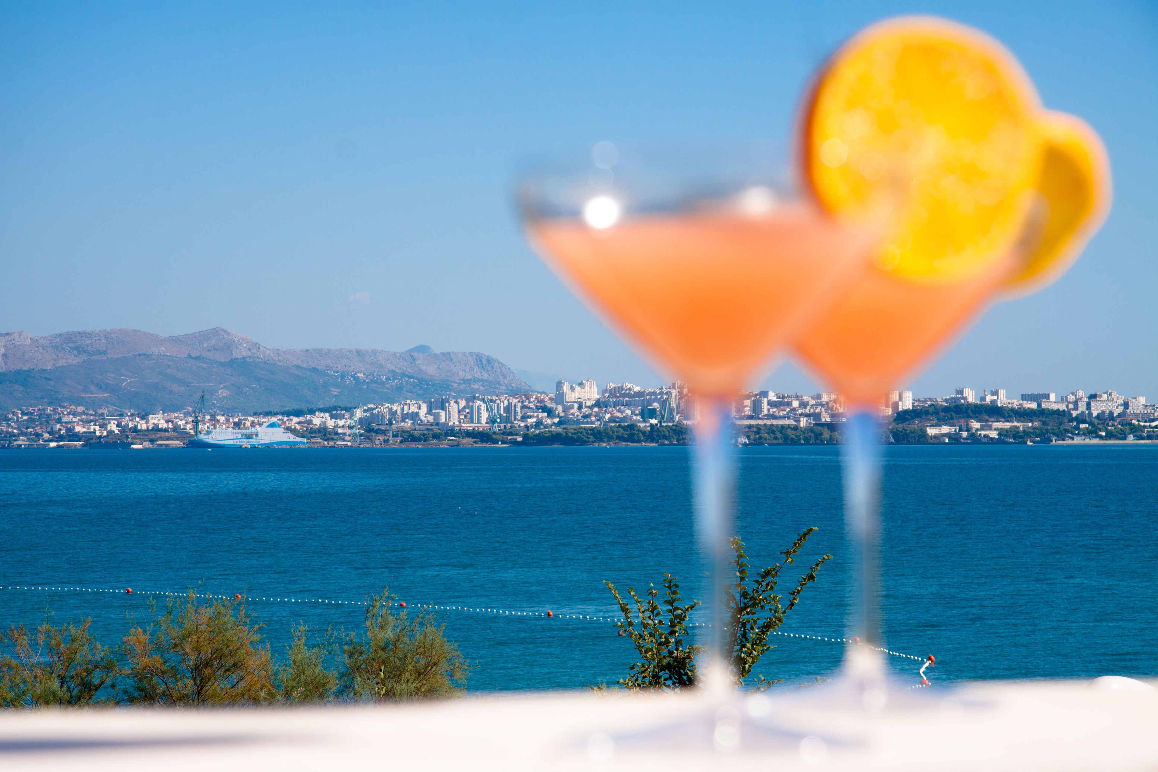Two martini glasses with heart-shaped garnishes in the foreground, with a cityscape and mountains in the background.