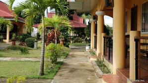 A covered walkway with palm trees and potted plants, leading to a building with a red-tiled roof. - Villa Manuel Tourist Inn (Puerto Princesa)