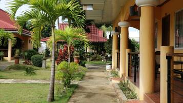 A covered walkway with palm trees and potted plants, leading to a building with a red-tiled roof.