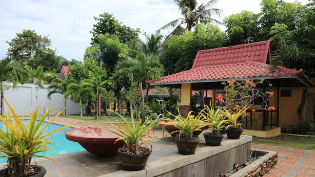 A pool area with potted plants, a red-roofed structure, and a brick pathway. - Villa Manuel Tourist Inn (Puerto Princesa)