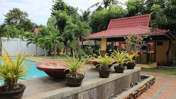 A pool area with potted plants, a red-roofed structure, and a brick pathway.