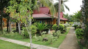A house with a red tiled roof, surrounded by lush greenery and a concrete pathway. - Villa Manuel Tourist Inn (Puerto Princesa)