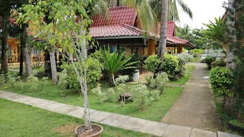 A house with a red tiled roof, surrounded by lush greenery and a concrete pathway.