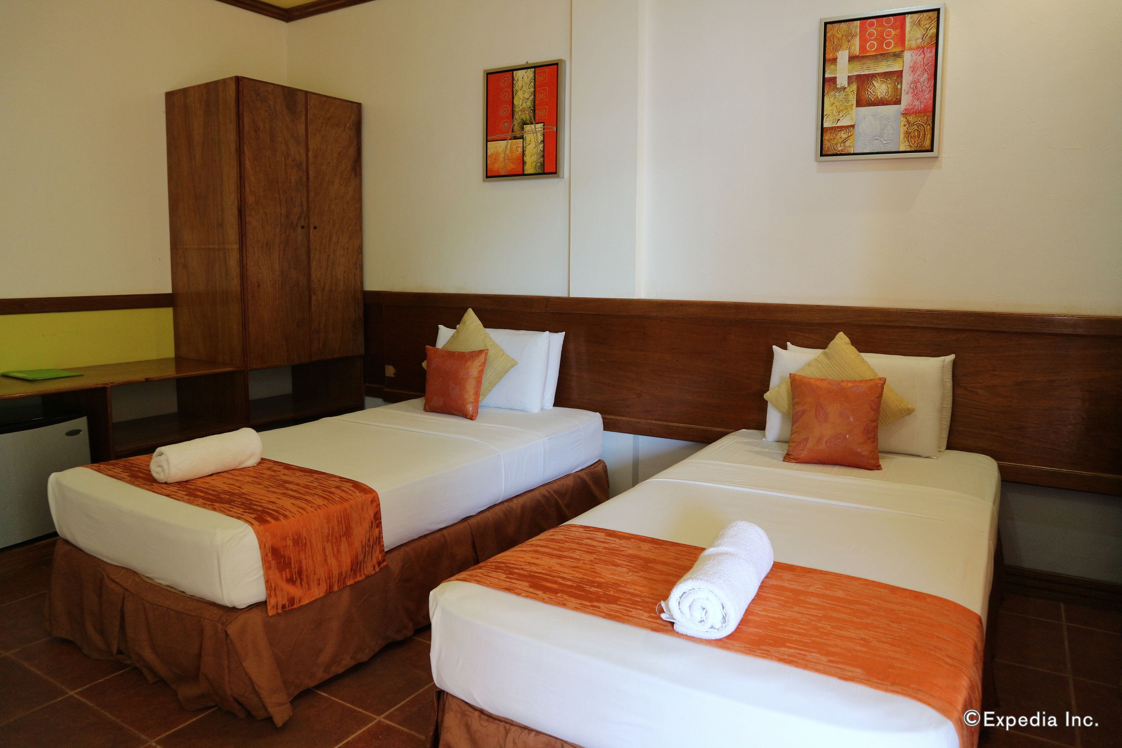 Two single beds with brown headboards, white linens, and orange throw blankets.