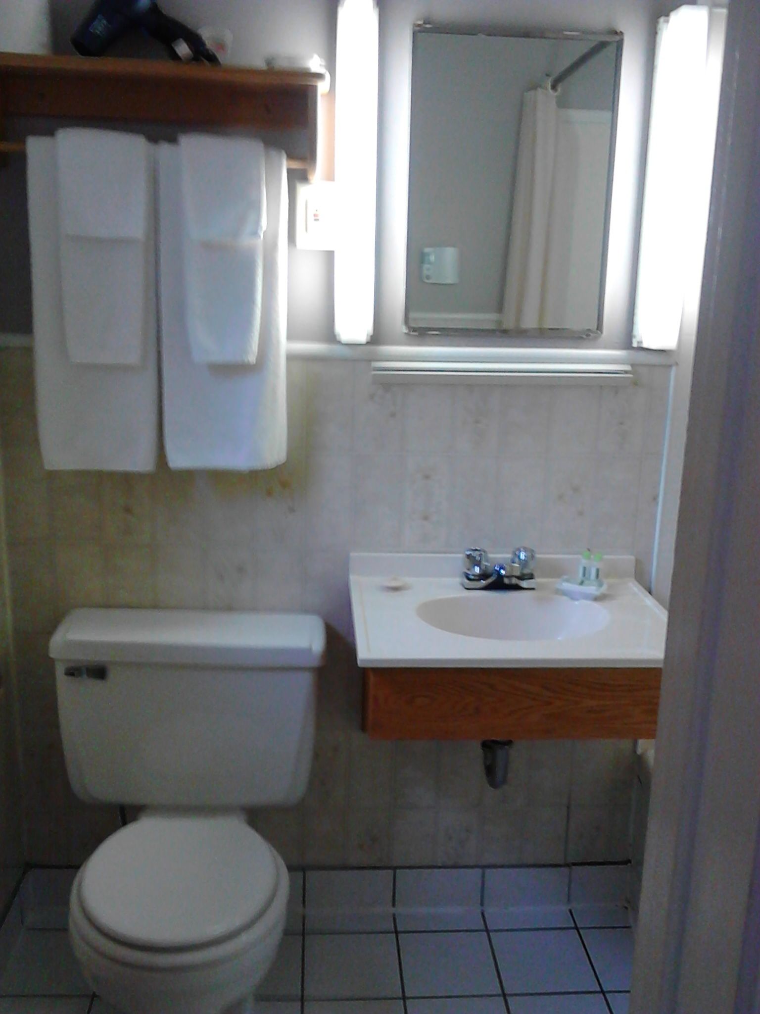 A small bathroom with a toilet, sink, and mirror. There are towels hanging on a rack above the toilet.