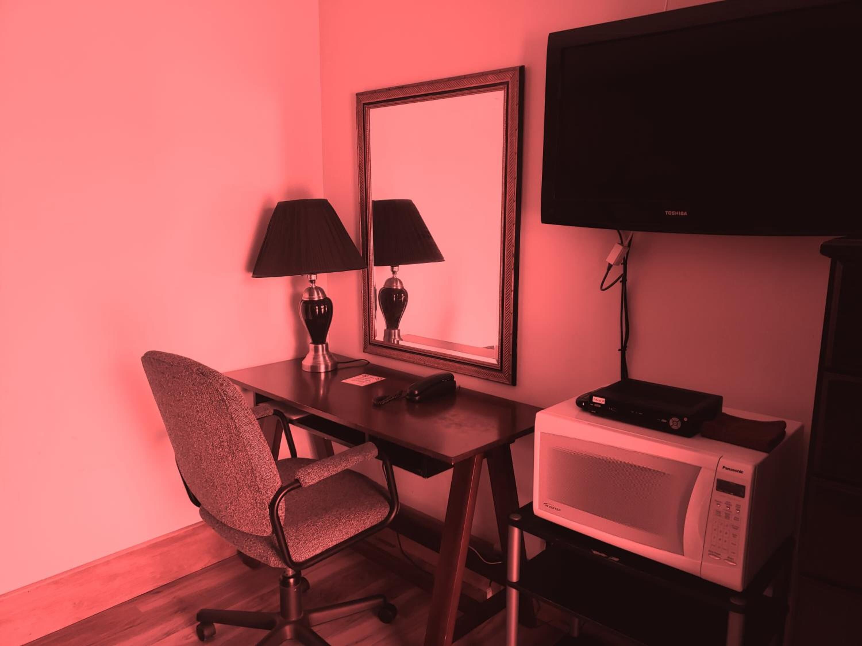 Una camera d'albergo con una scrivania, una sedia, una televisione, un forno a microonde e uno specchio.