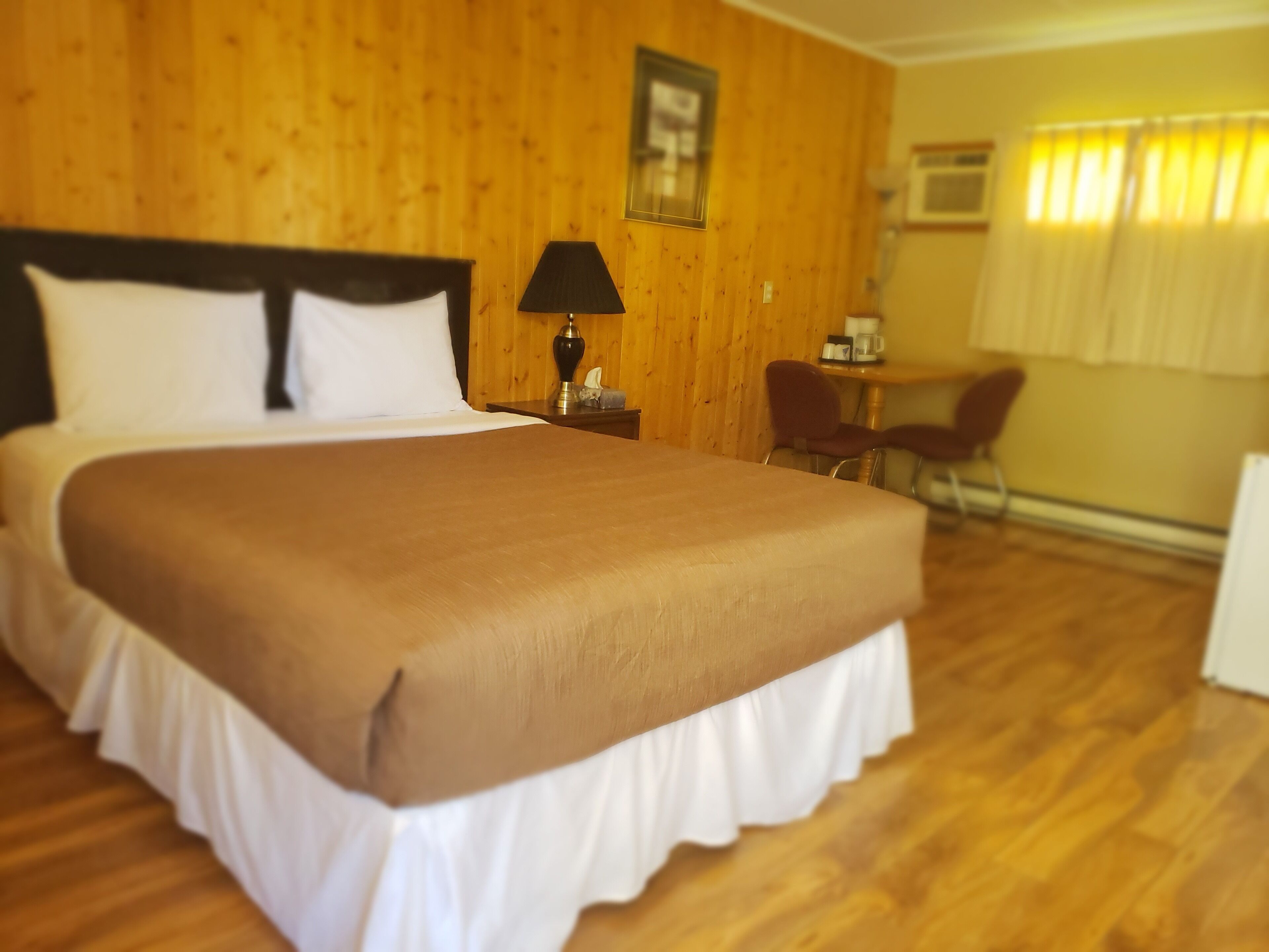 A hotel room with a large bed, wooden walls, a small table with a lamp, and a chair.