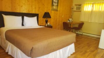 A hotel room with a large bed, wooden walls, a small table with a lamp, and a chair.