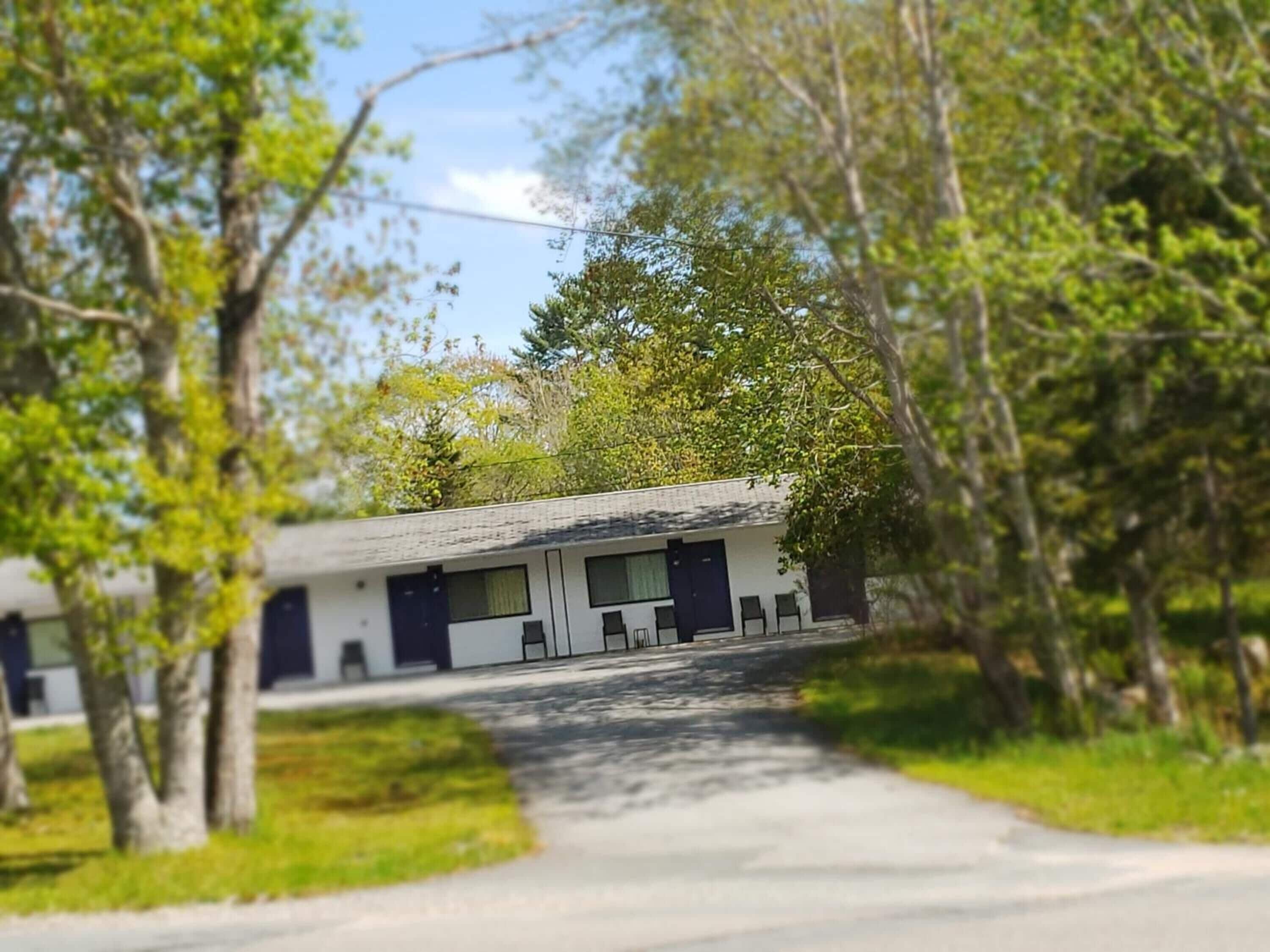Ein einfaches Motel mit eingeschossigem Bau, überdachtem Parkplatz und einem Weg zum Eingang.