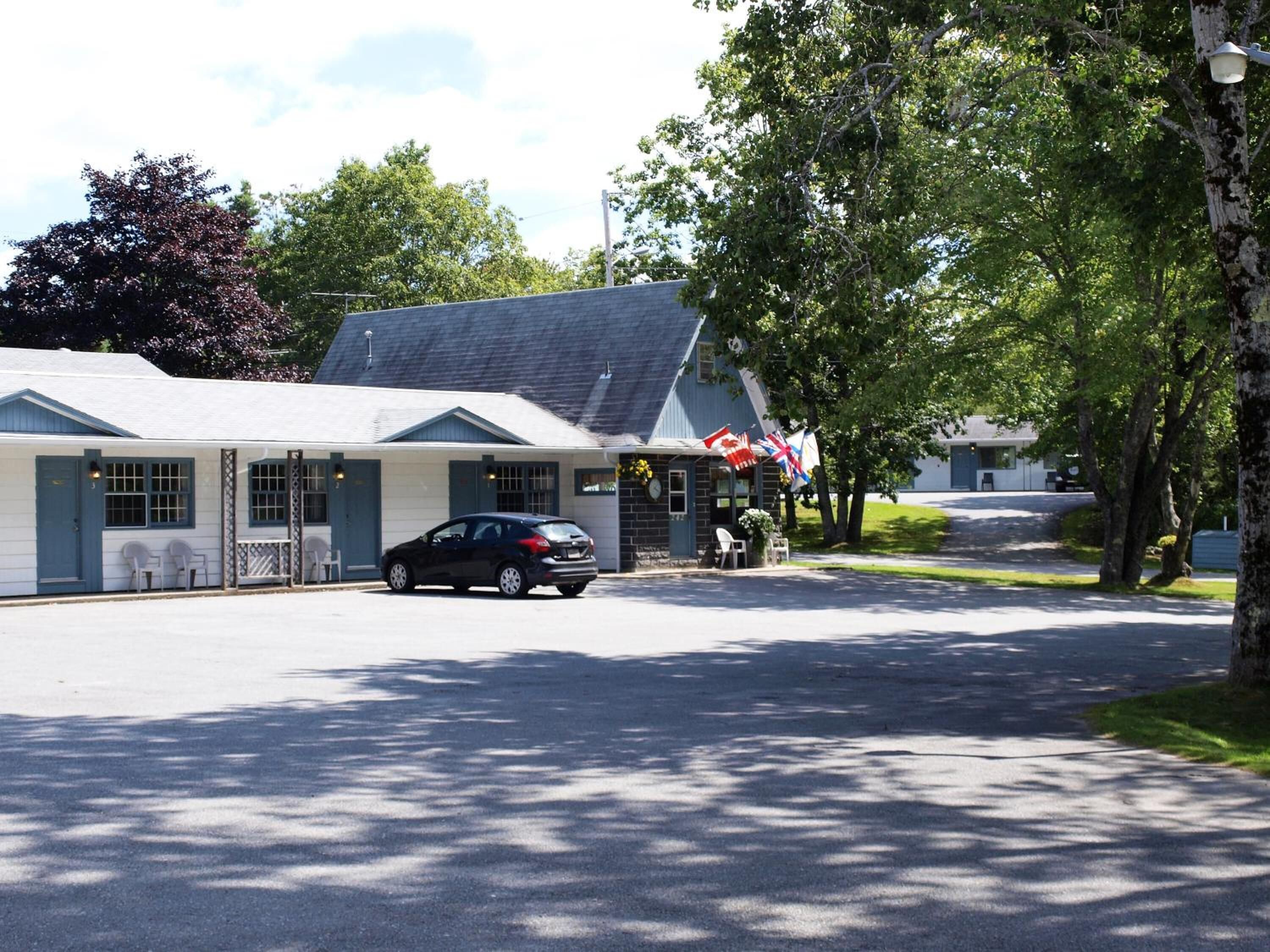 Un motel avec un bâtiment d’un seul étage, une voiture garée devant et un drapeau à l’extérieur.