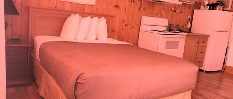 Un dormitorio con una cama grande, paredes de madera, una pequeña kitchenette y un cuadro enmarcado en la pared.