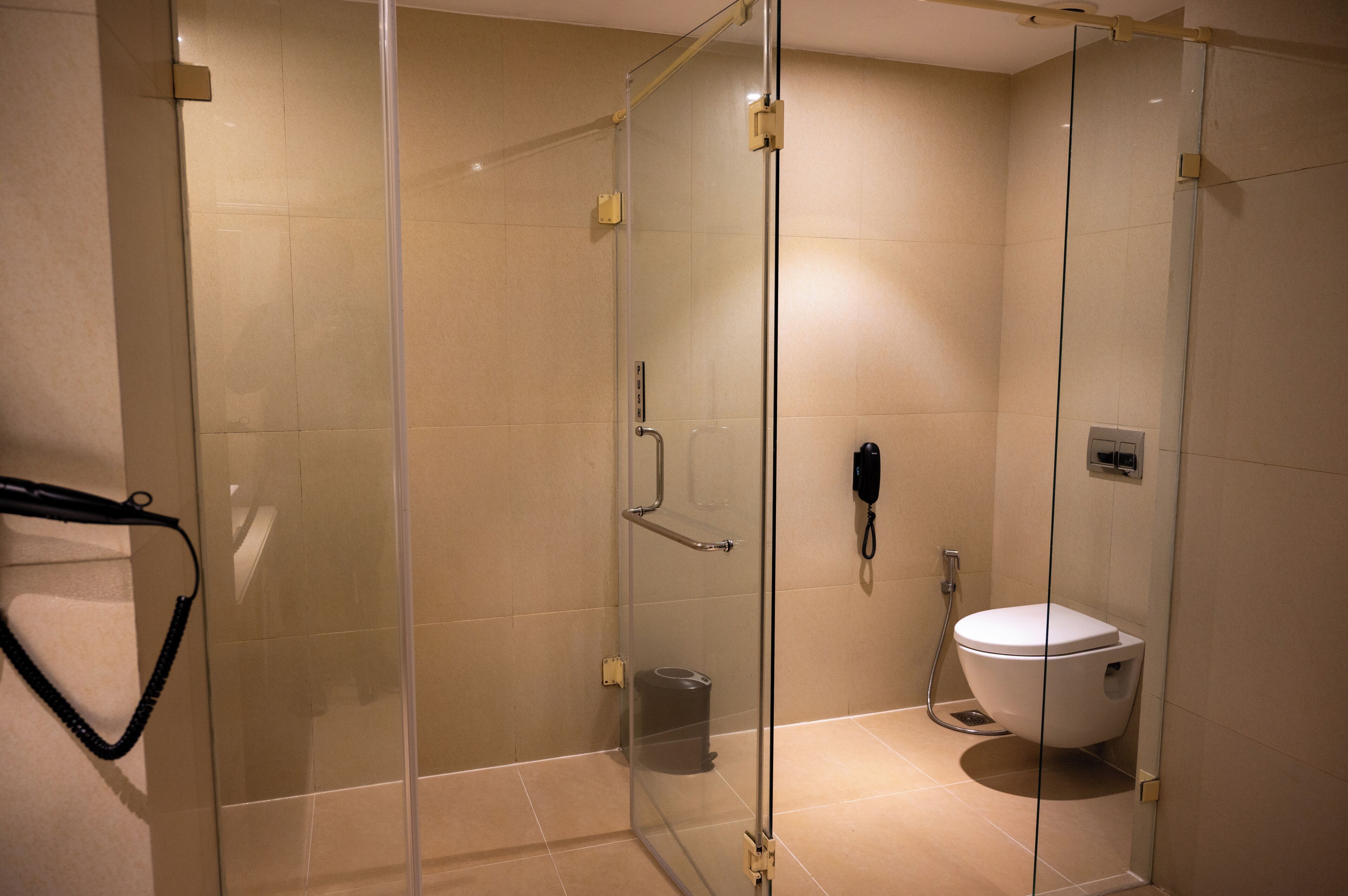 A glass-enclosed shower stall with a toilet and a phone.