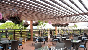 Un espacio al aire libre con mesas y sillas, macetas colgantes y una pérgola de madera.