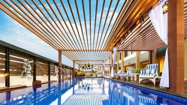 Una piscina interior moderna con suelo de baldosas azules brillantes, techo de listones de madera y sillones de descanso a un lado.