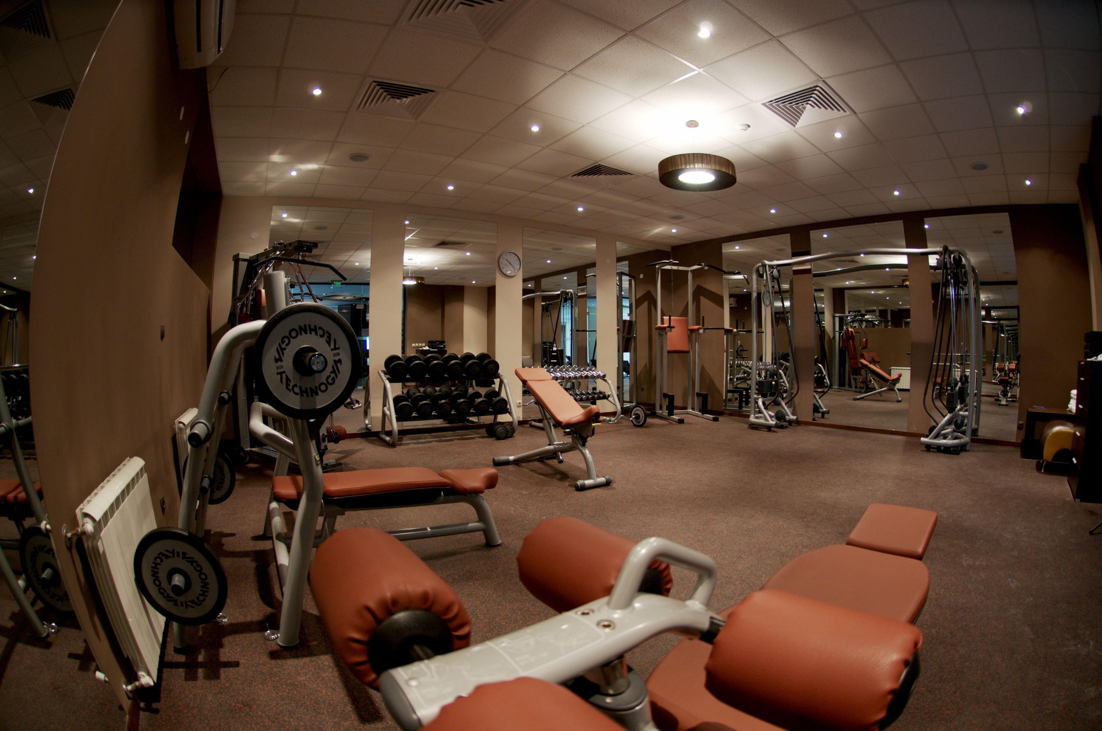 Ett gym med olika typer av träningsutrustning, inklusive bänkar, hantlar och styrketräningsmaskiner.