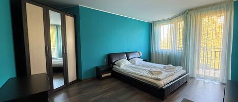 A bedroom with a bed, a wardrobe, a nightstand, and a window with curtains.