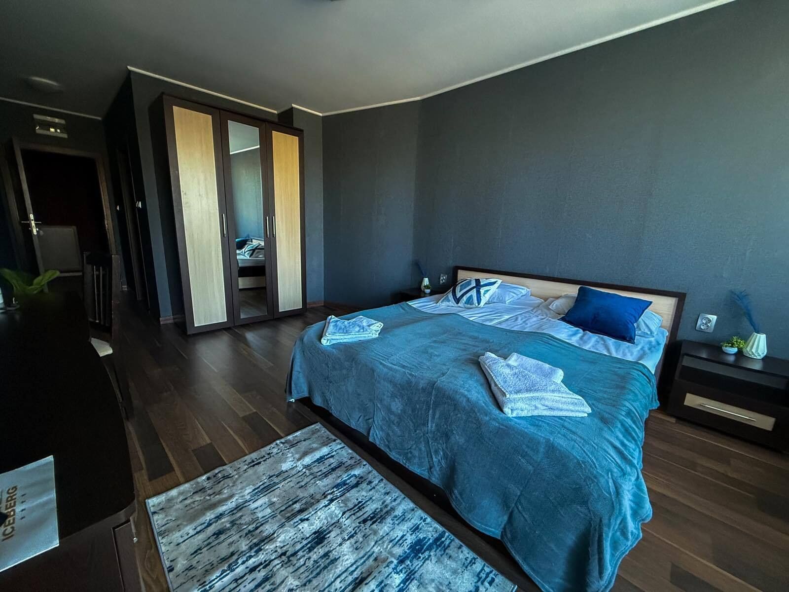 A modern bedroom with a large bed, a walk-in closet, and a view of a balcony.