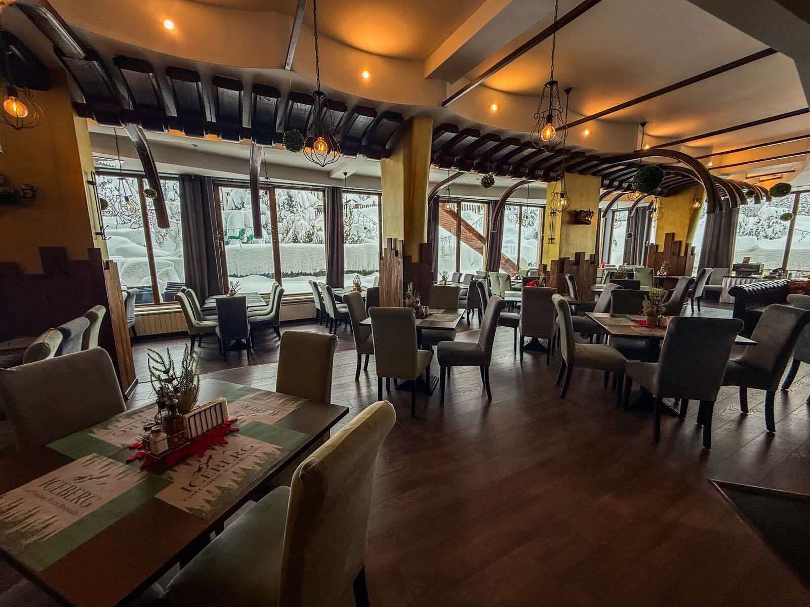 Een restaurant met een modern interieur, met houten tafels en stoelen, grote ramen met uitzicht op een besneeerd landschap en hangende吊灯.